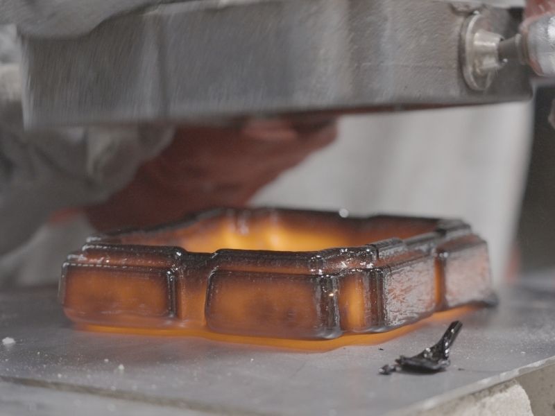 A freshly cast lava tray designed by Max Greiner glows orange beneath its darkening surface as a metal mould is lifted away.