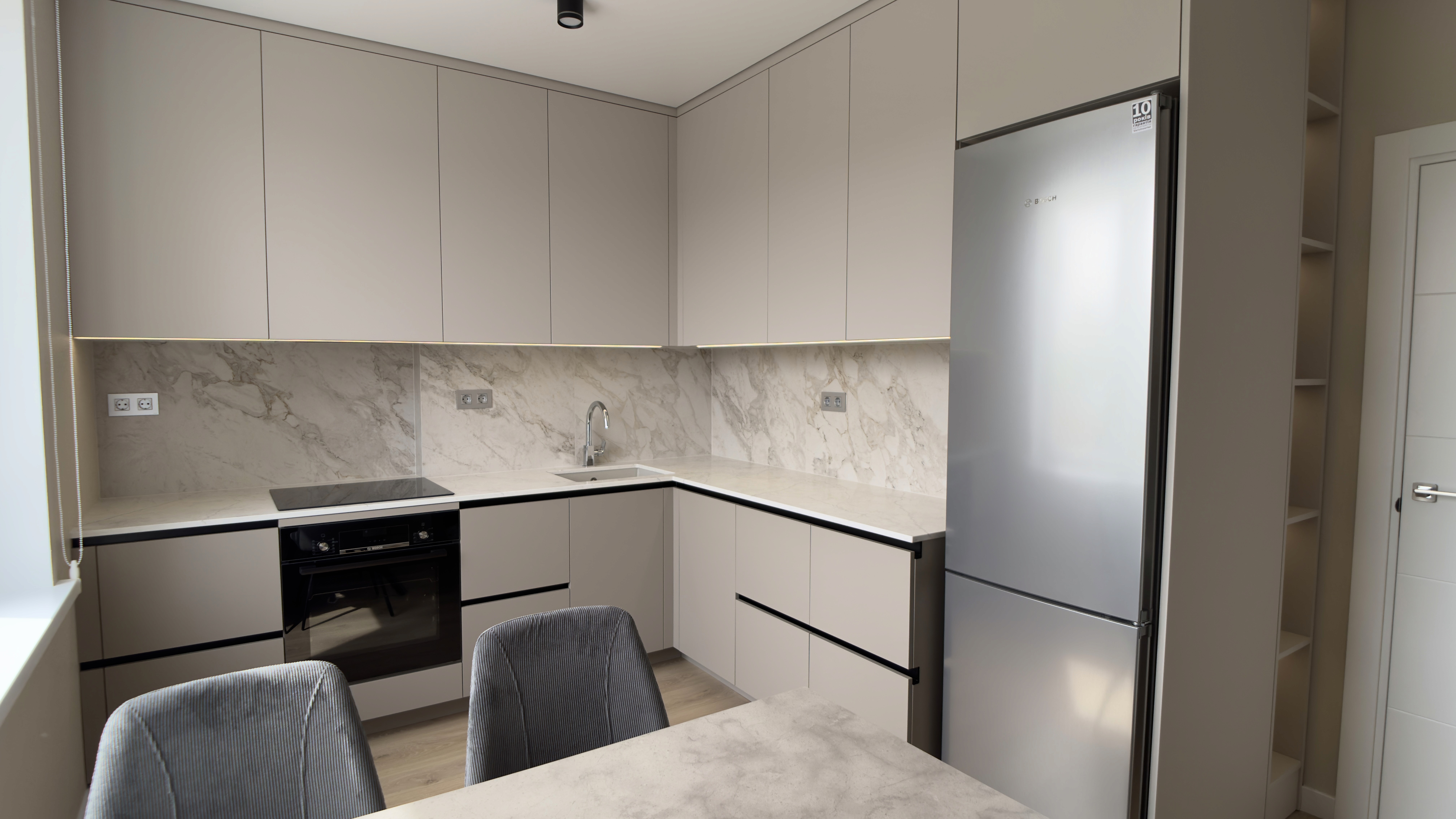 Кутова кухня з мармуровим фартухом, сірими фасадами та великою кількістю місць для зберігання