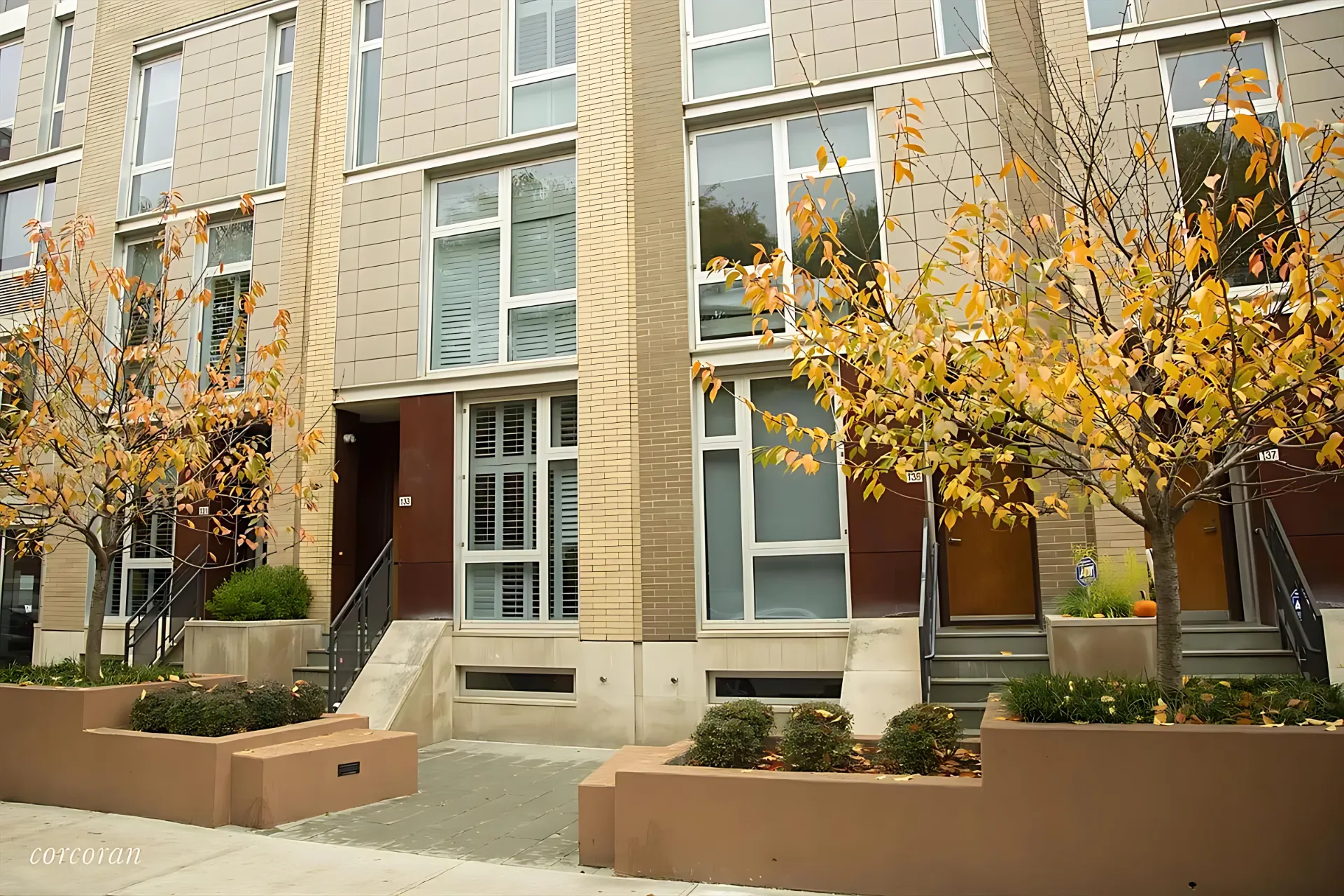 A row of brown brick buildings with green trees in front, creating a pleasant urban landscape.