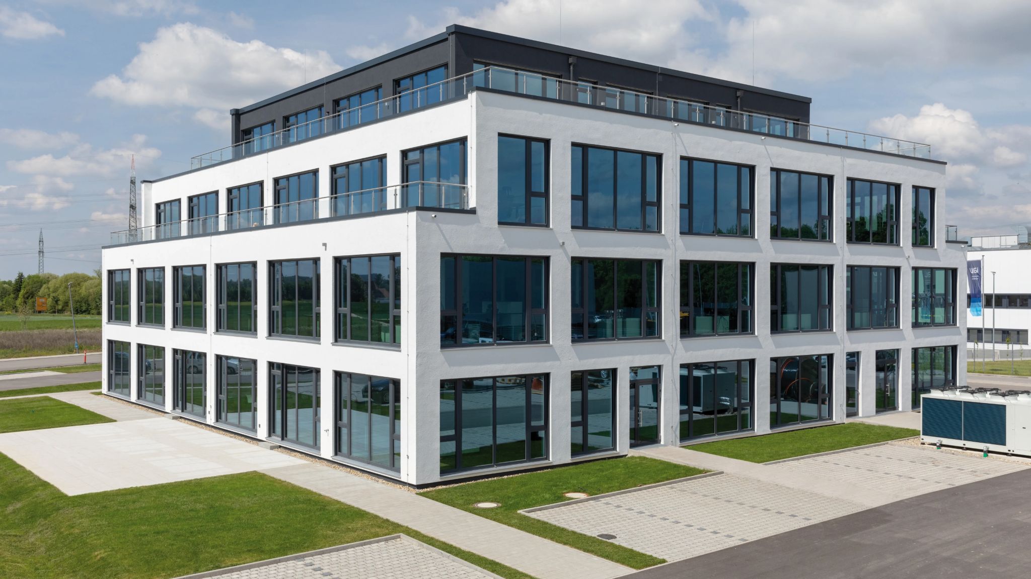 Blick auf modernes Bürogebäude mit Parkplatz davor.