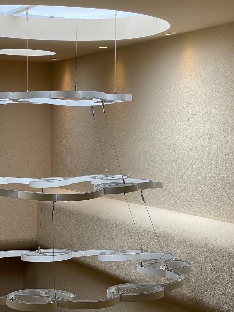 Modern white chandelier hanging from the ceiling, with circular designs and soft lighting against a textured beige wall.