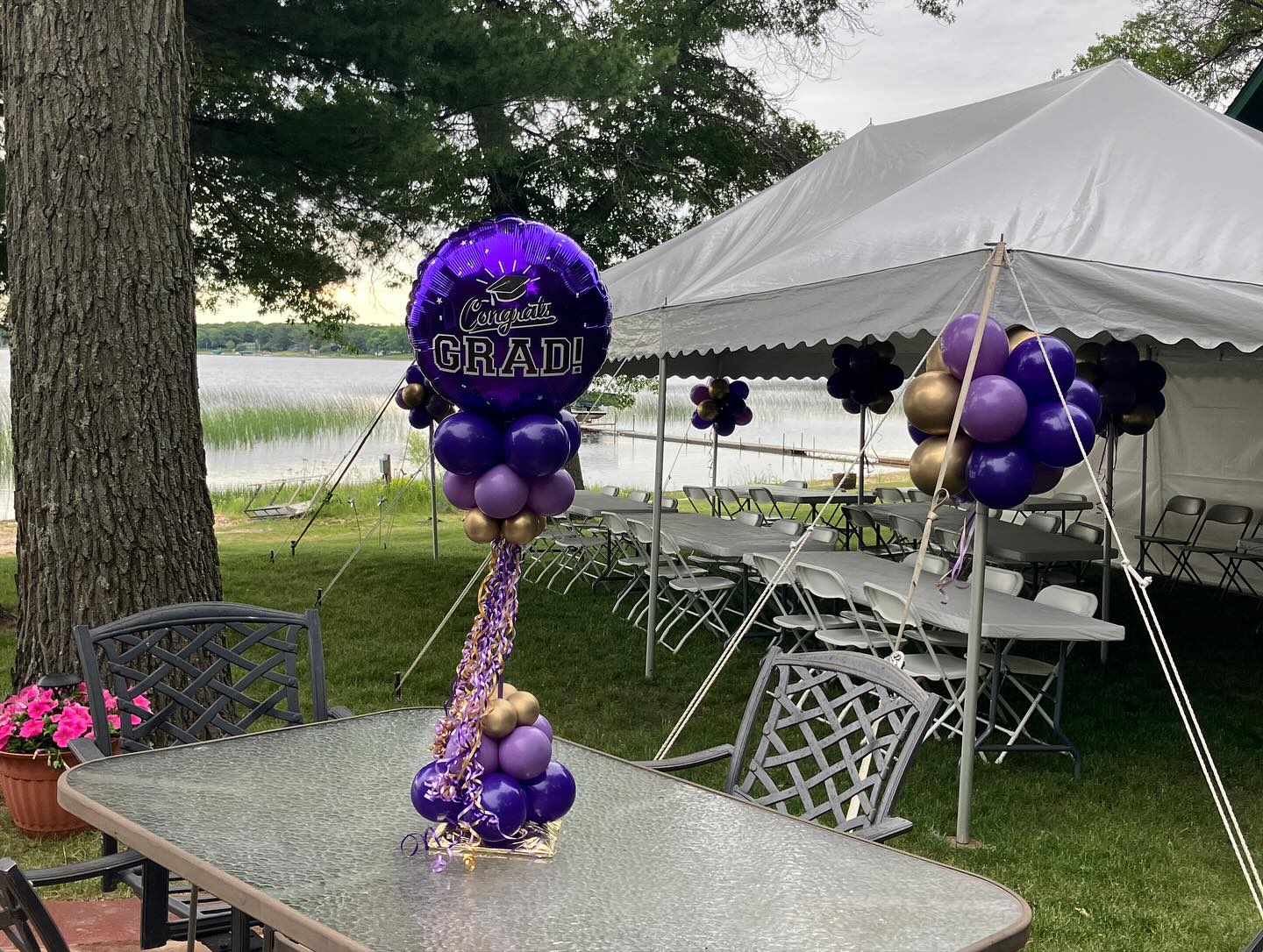Purple and gold balloon centerpiece featuring a graduation cap topper placed under a white event tent by Be Bold Balloons