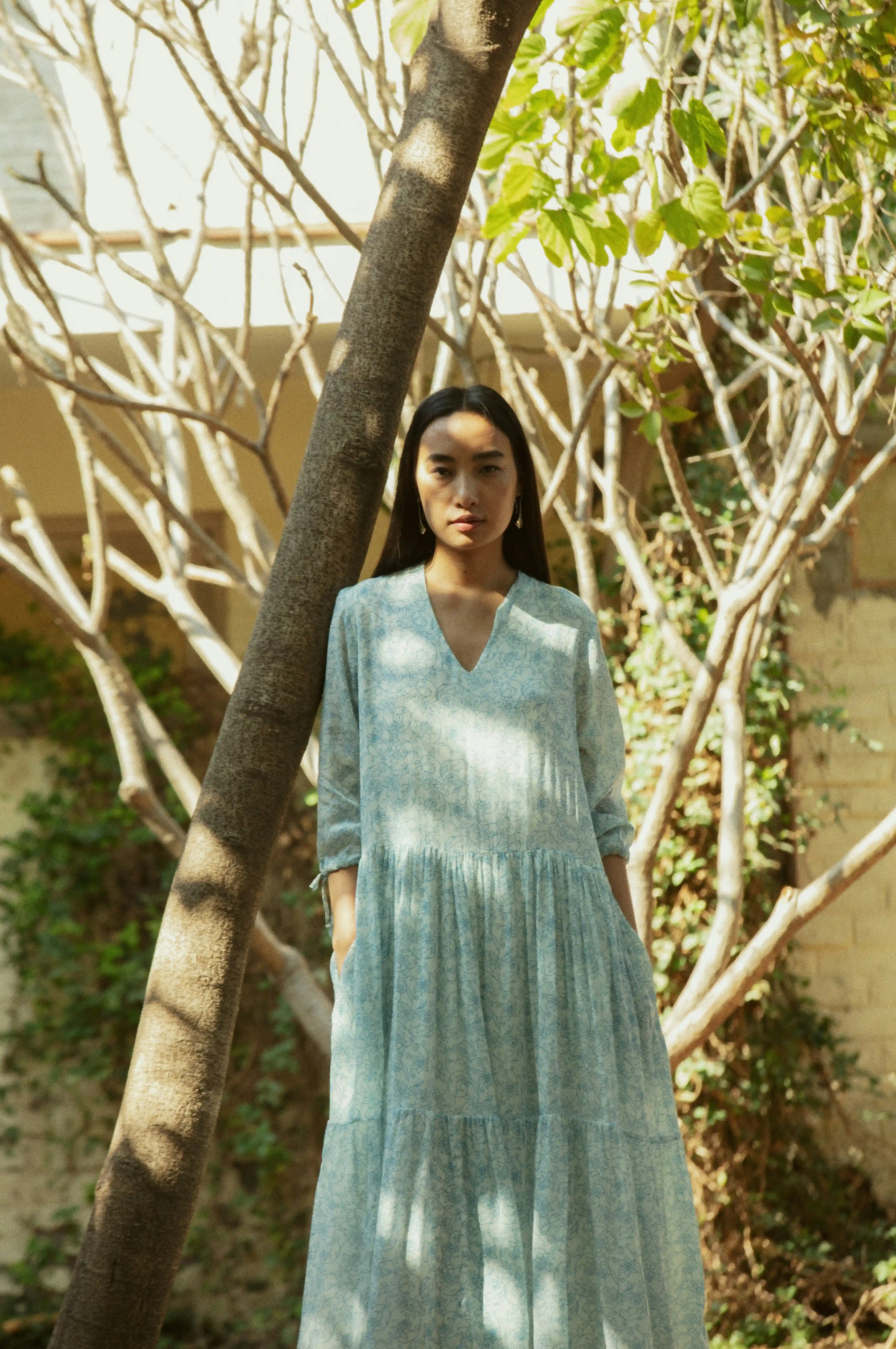 Woman wearing light blue floral dress standing in front of decorative trees.