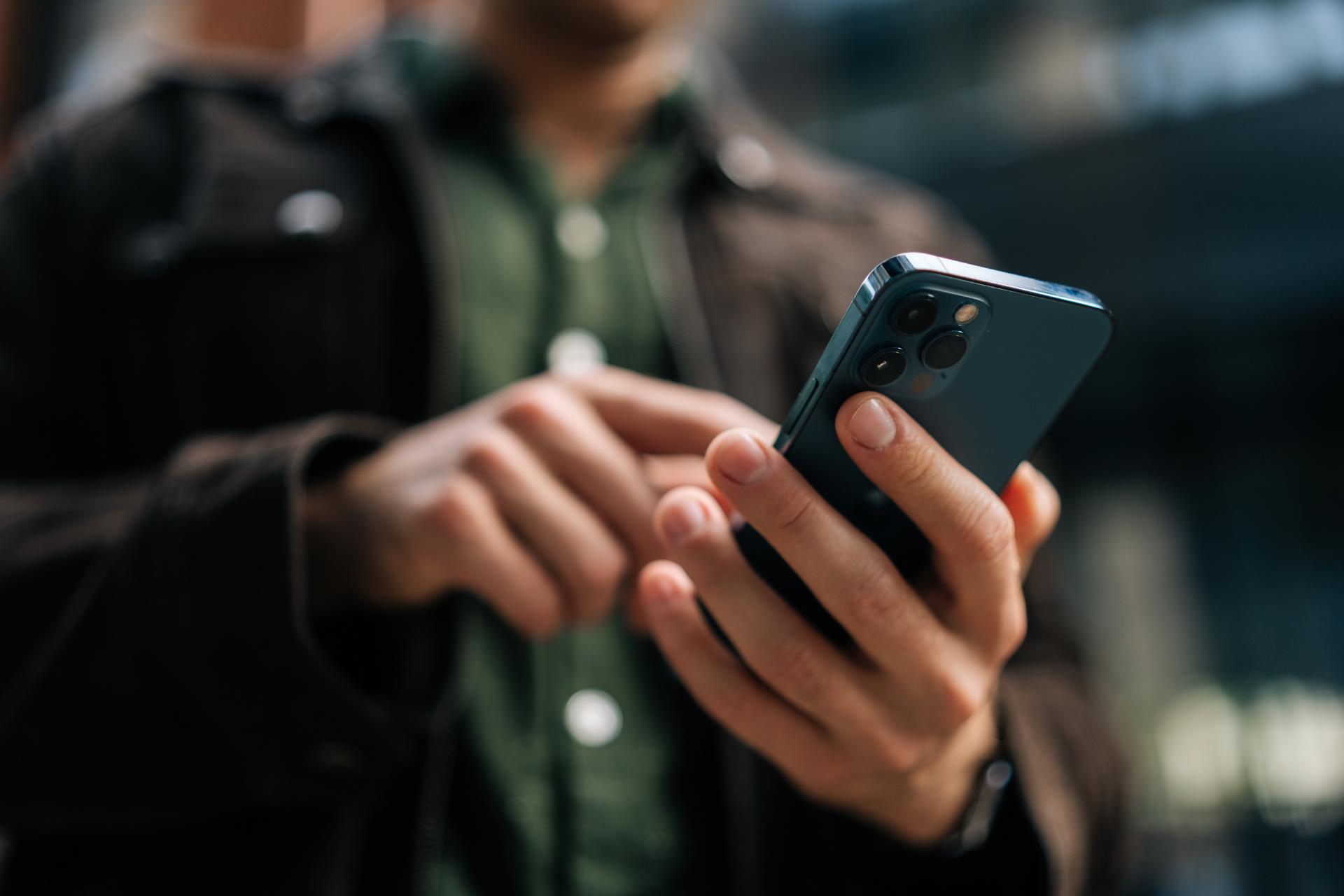 Close up hands of unrecognizable man holding and using smartphone standing on city street