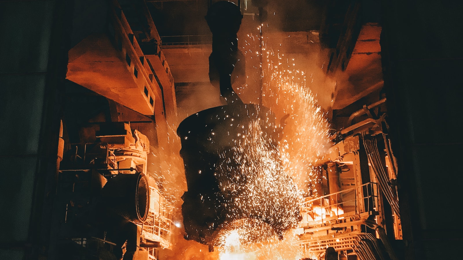 Steel production machinery throwing orange sparks inside a dark mill