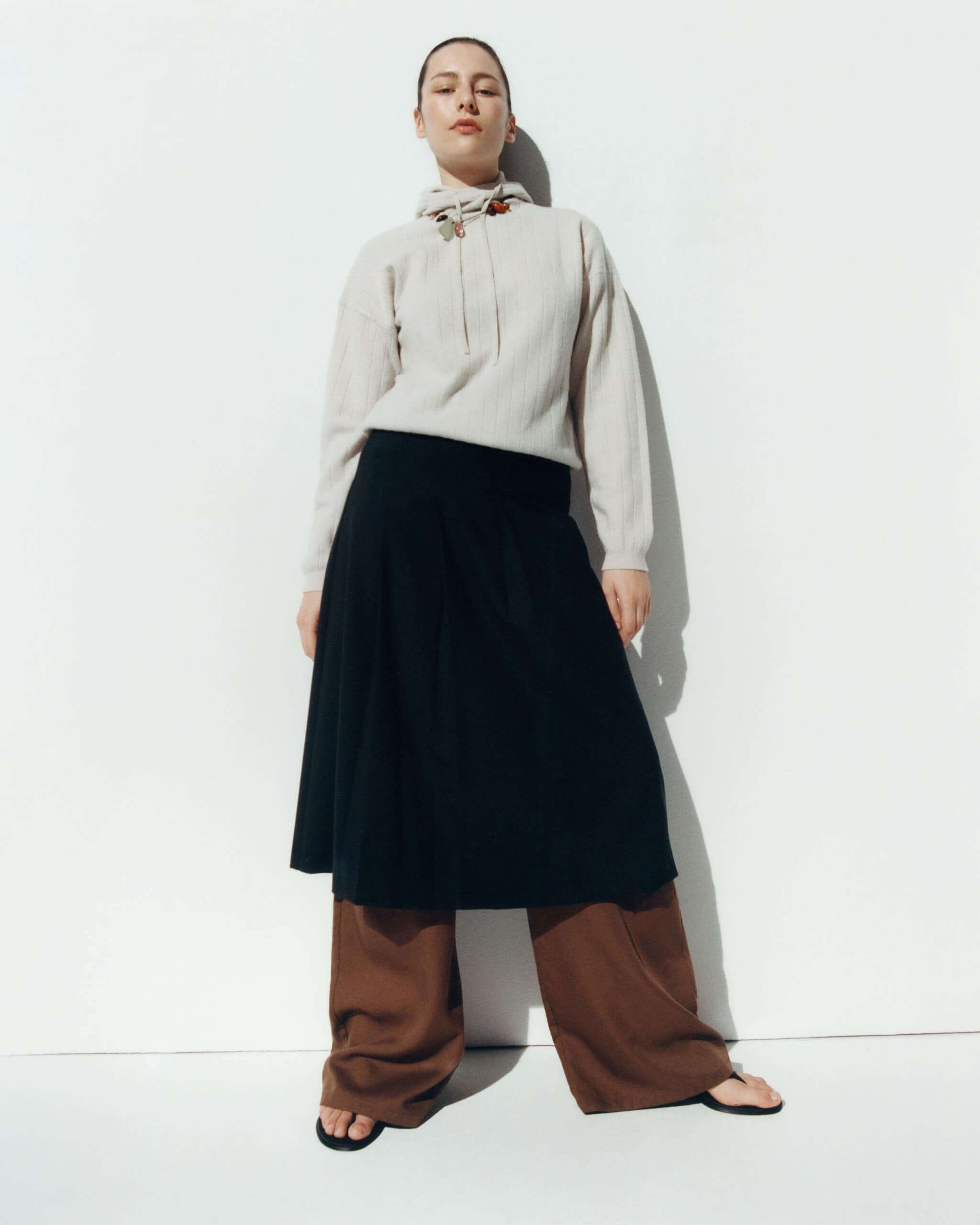 Une mannequinporte hoodie gris, jupe noir et pantalon marron