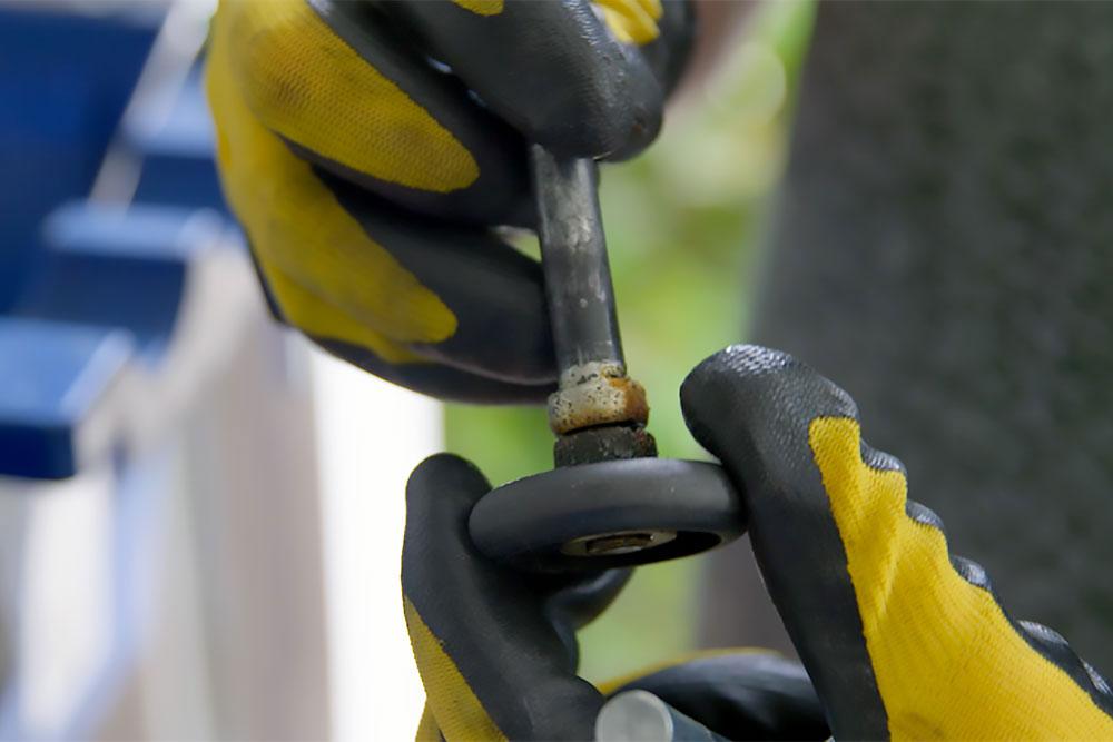 Technician inspecting a rusted garage door roller and axle for seasonal maintenance in Northwest Arkansas | Northwest Arkansas Garage Door Repair & Installation