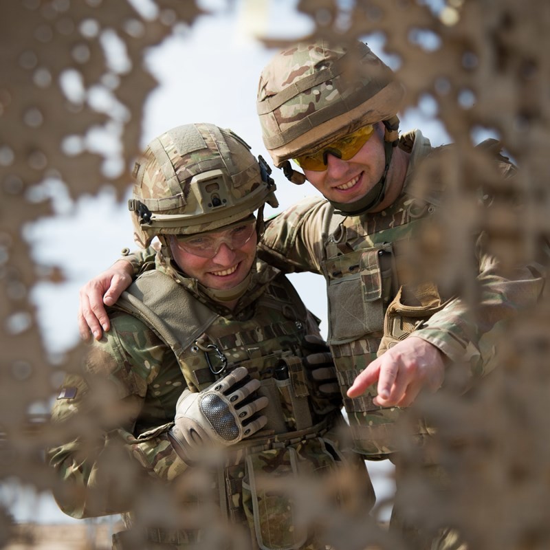 Photo of to soilders in full desert gear with arms around each other smiling at the camera