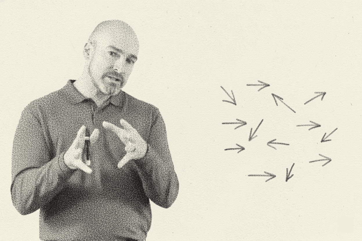 A monochrome image of a man, identified as a Gino Wickman discussing the Entrepreneurial Operating System (EOS), standing next to a hand-drawn diagram. The diagram shows multiple arrows, representing people and their focus, pointing in conflicting, random directions, illustrating how most organizations lack alignment. The speaker is demonstrating this concept with his hands.