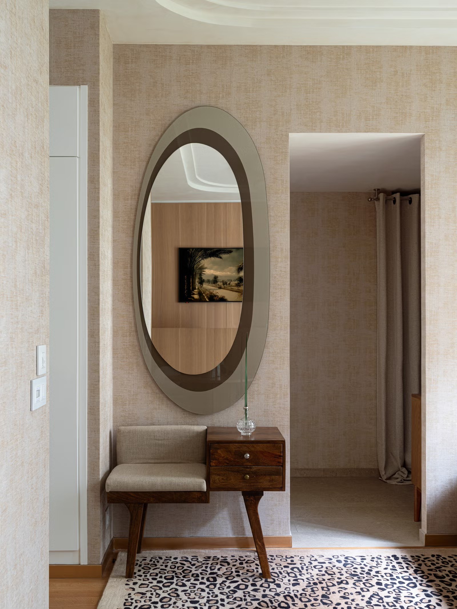 Zoom sur un grand miroir ovale au cadre noir posé sur un revêtement mural à texture minérale beige.