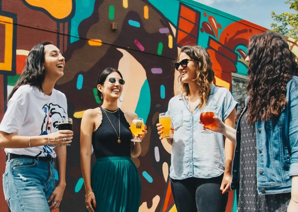 Group of friends having a drink together against a colourful wall mural