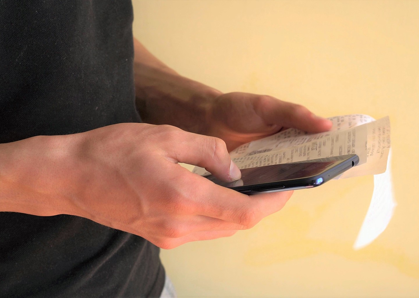 Una persona tiene in una mano il suo smartphone con il software gestione spese e nell'altra mano degli scontrini