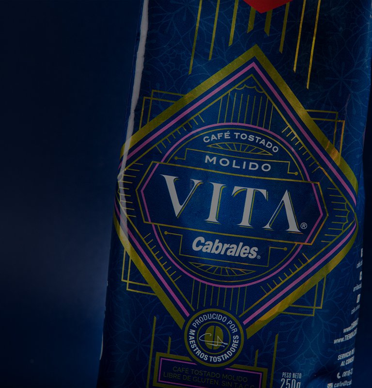 Close-up of a coffee package labeled "Vita Cabrales" in bold white text on a blue geometric pattern background. The tone is vibrant and elegant.