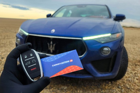 CarKeyAction technician holding a car key and business card in front of a Maserati after on-site car key service