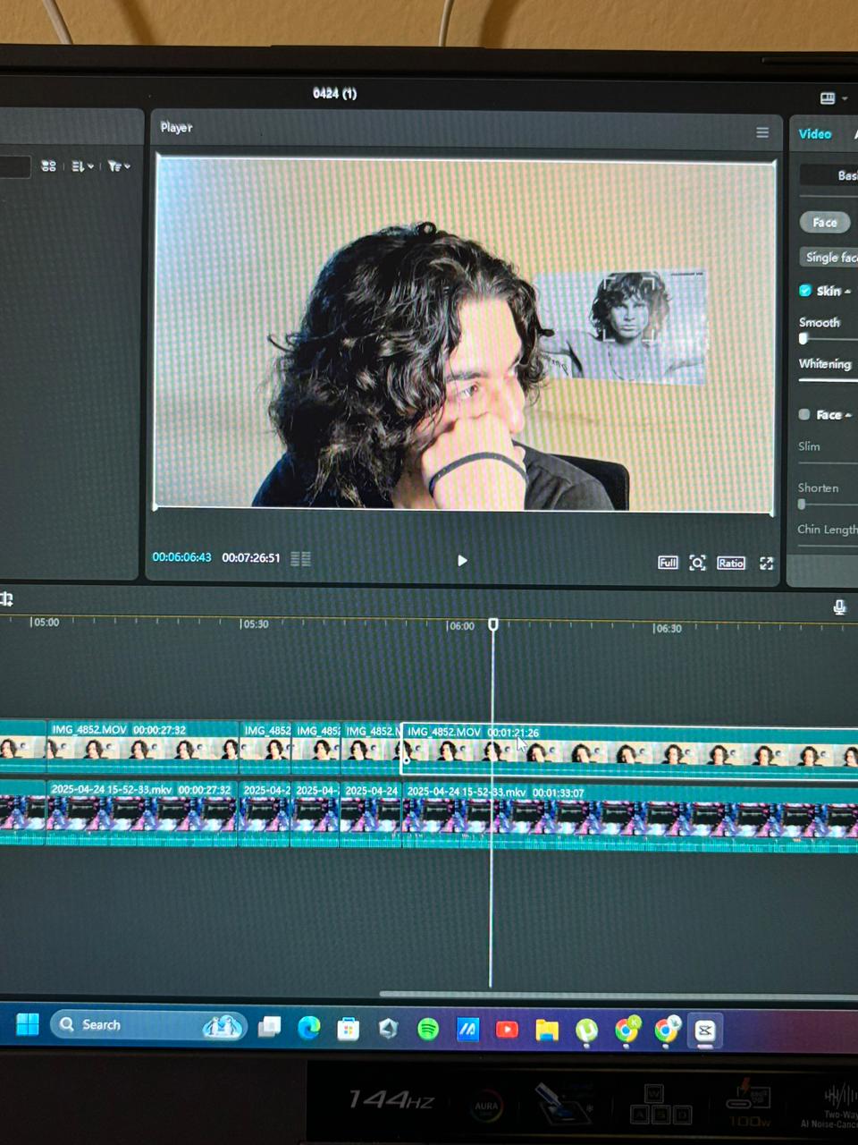 Una persona con una camiseta negra y pantalones de color claro está de pie en la cima rocosa de una montaña al atardecer, sosteniendo una cámara frente a su cara para tomar una foto. Un mar de nubes se extiende detrás de ellos, iluminado por la luz dorada del sol poniente.