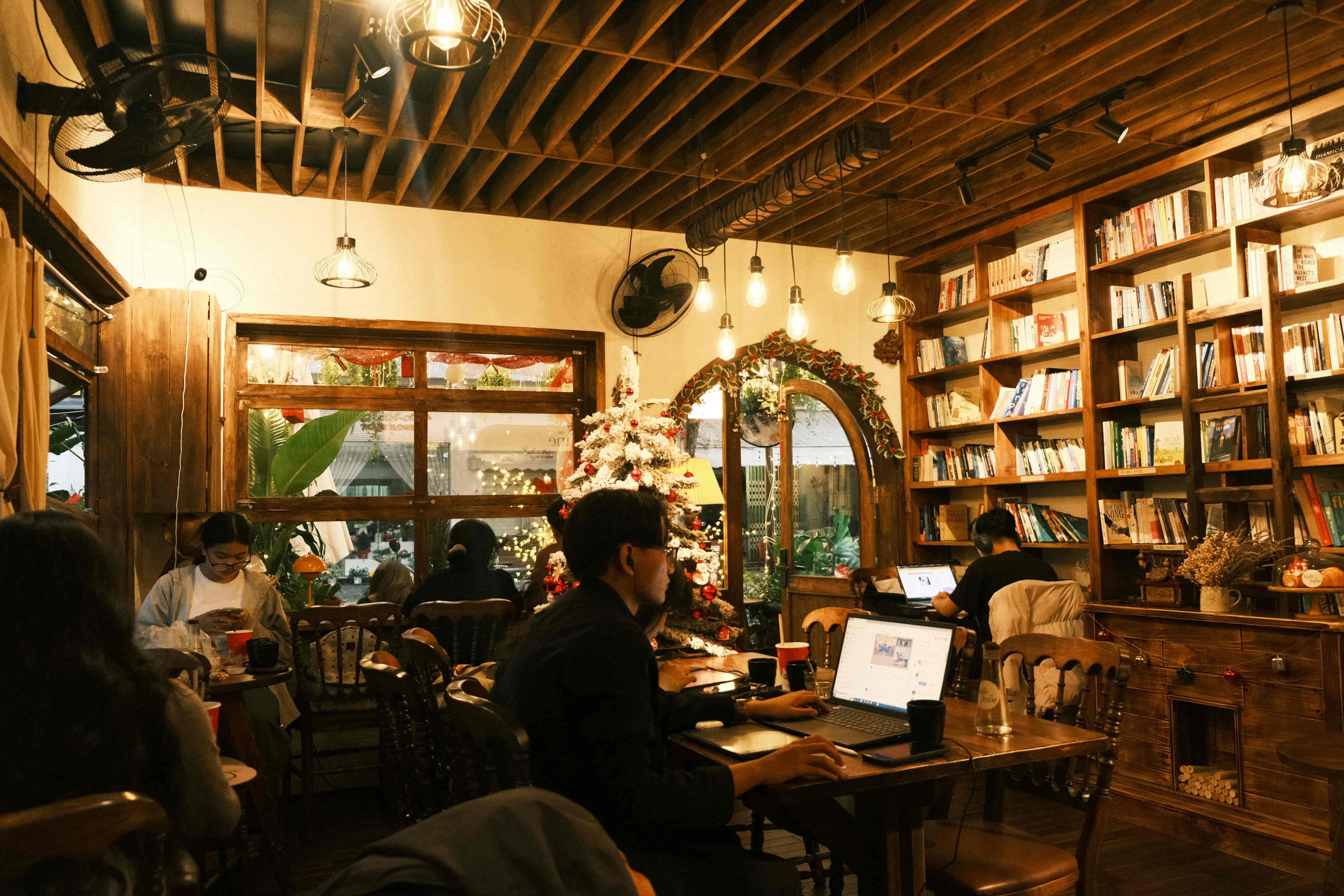 Cozy coffee shop with bookshelves, Christmas decor, and people working on laptops.