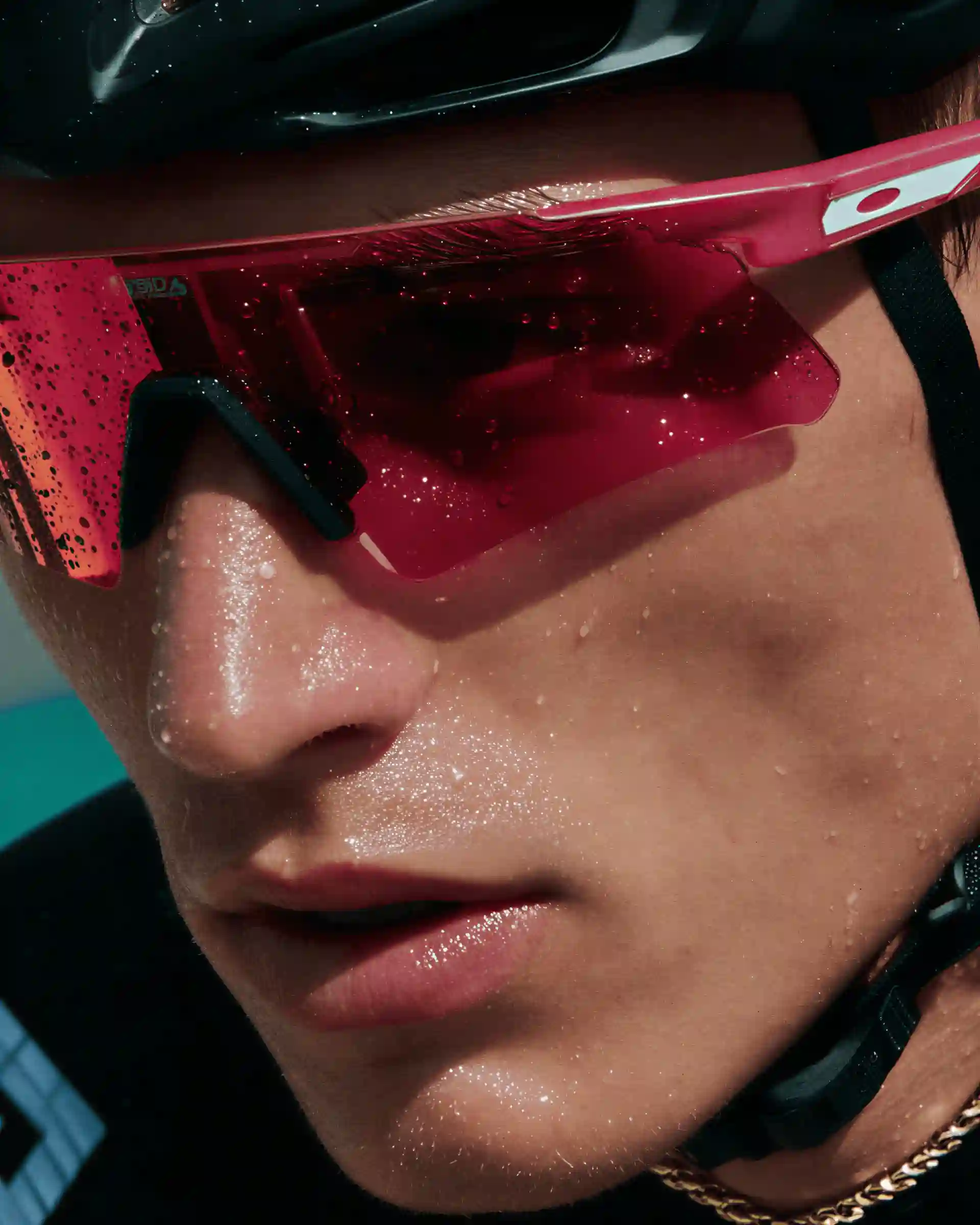 Close-up of an athlete wearing red sports sunglasses and a helmet, with sweat drops on their face.