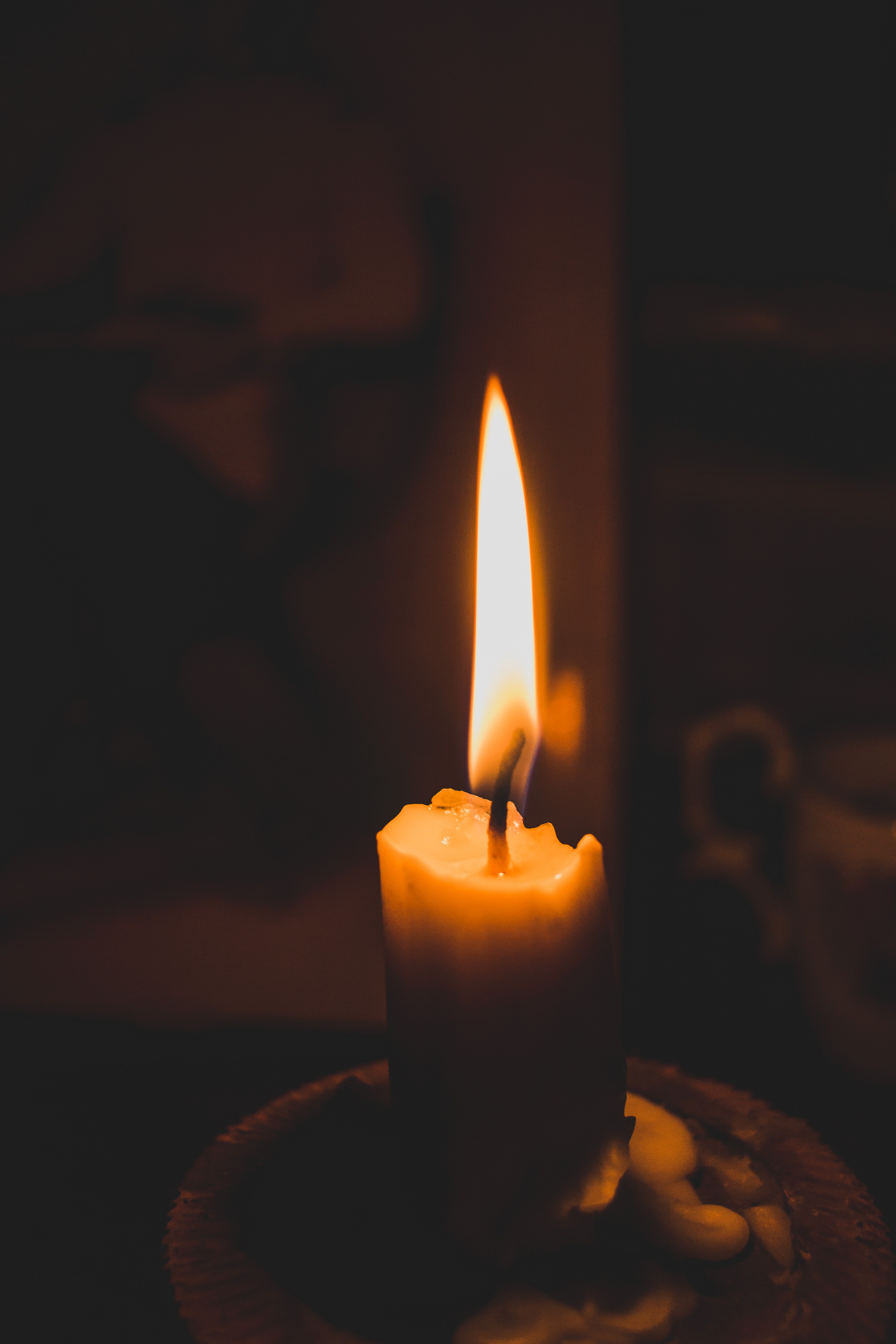A single candle flickering in a dark setting, casting soft light and shadows around it.
