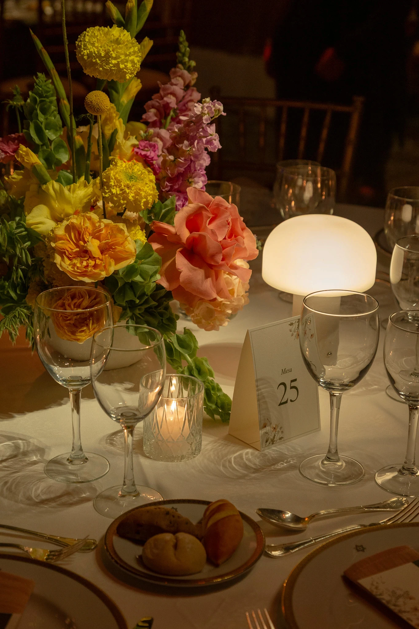Arreglo floral de mesa con rosas durazno, craspedias amarillas y lámpara de diseño en forma de hongo.