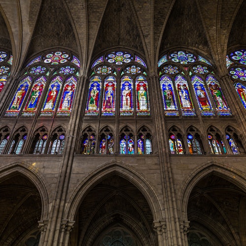 色彩繽紛的彩色玻璃窗描繪著各種場景和聖徒，位於一座宏偉的拱形大教堂內部。