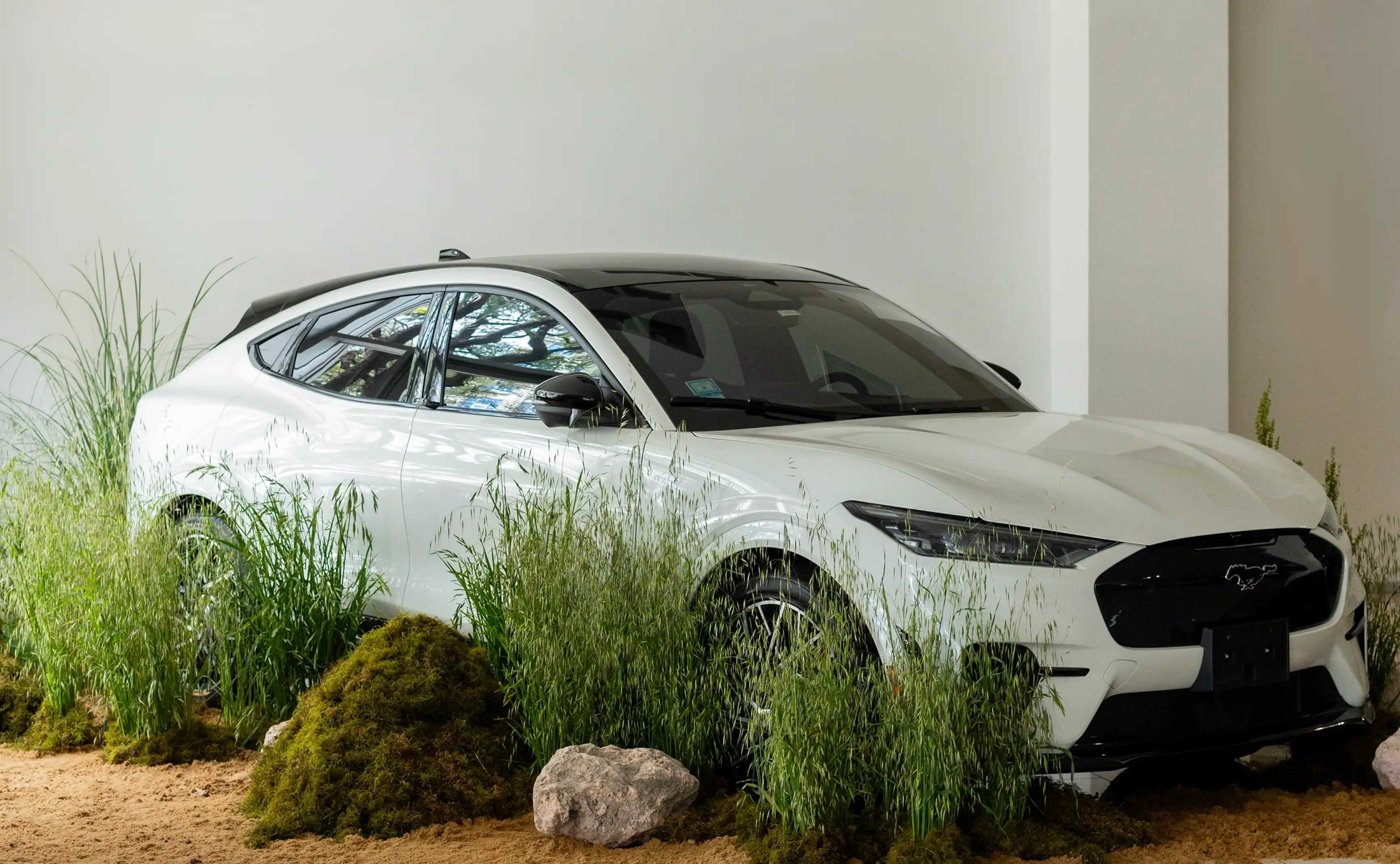 Automóvil eléctrico blanco exhibido entre pasto, musgo y rocas en instalación natural de interior.