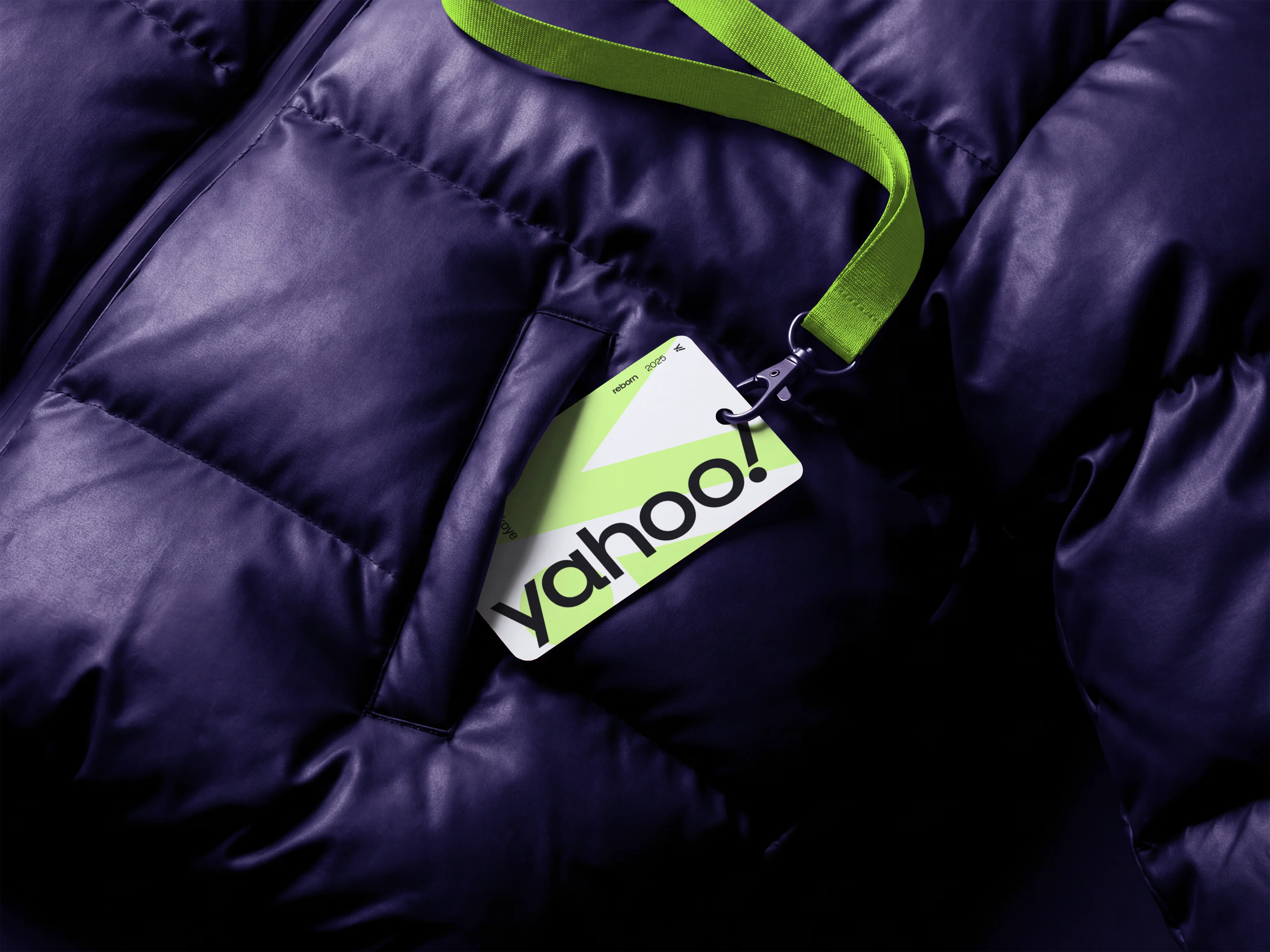 Badge Yahoo! vert fluo attaché à un cordon, posé sur une doudoune matelassée violet foncé.