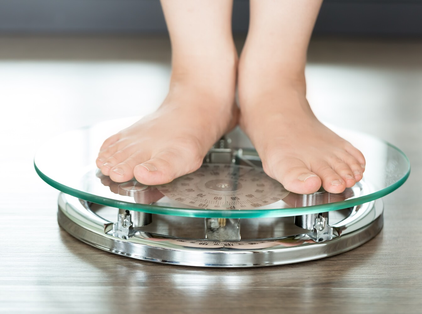woman standing on a glass scale in her bathroom to check her results from losing weight without exercising