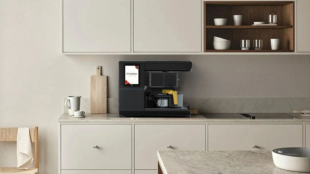 Posha automatic cooking system with touchscreen and cooking pot on a minimalist kitchen countertop, illustrating a full cooking system versus a self-cooking pot.