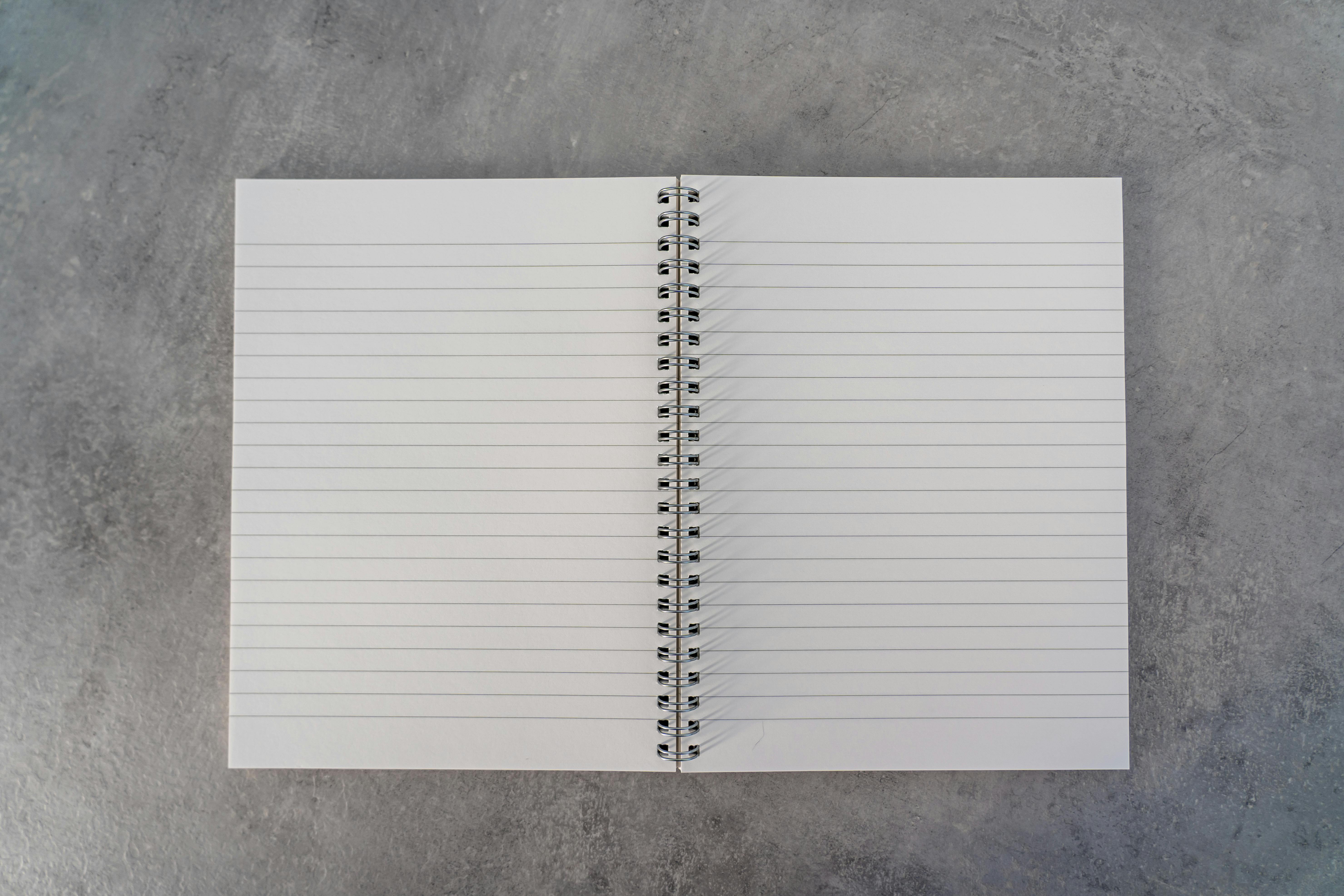 Open spiral-bound notebook with blank lined pages placed on a gray textured surface.