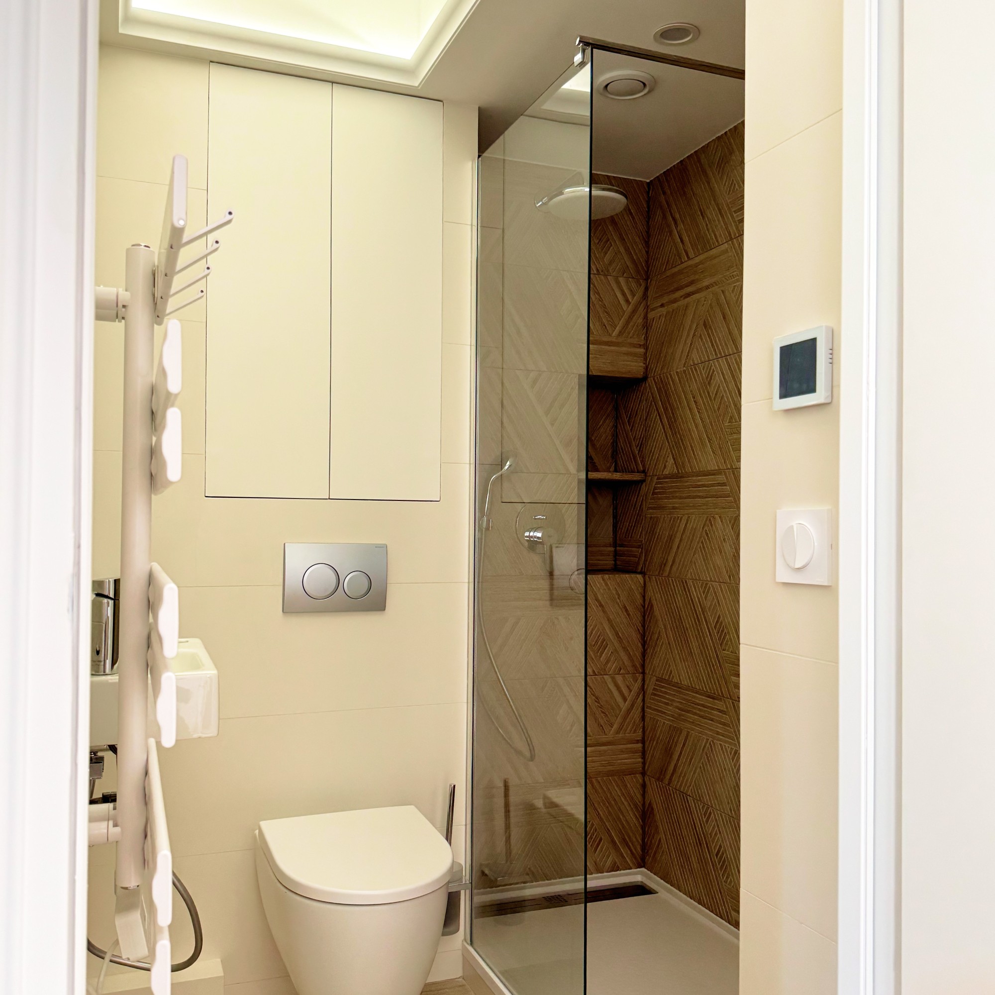 Vue de la douche et des WC suspendus avec finitions chromées et revêtement mural minéral.