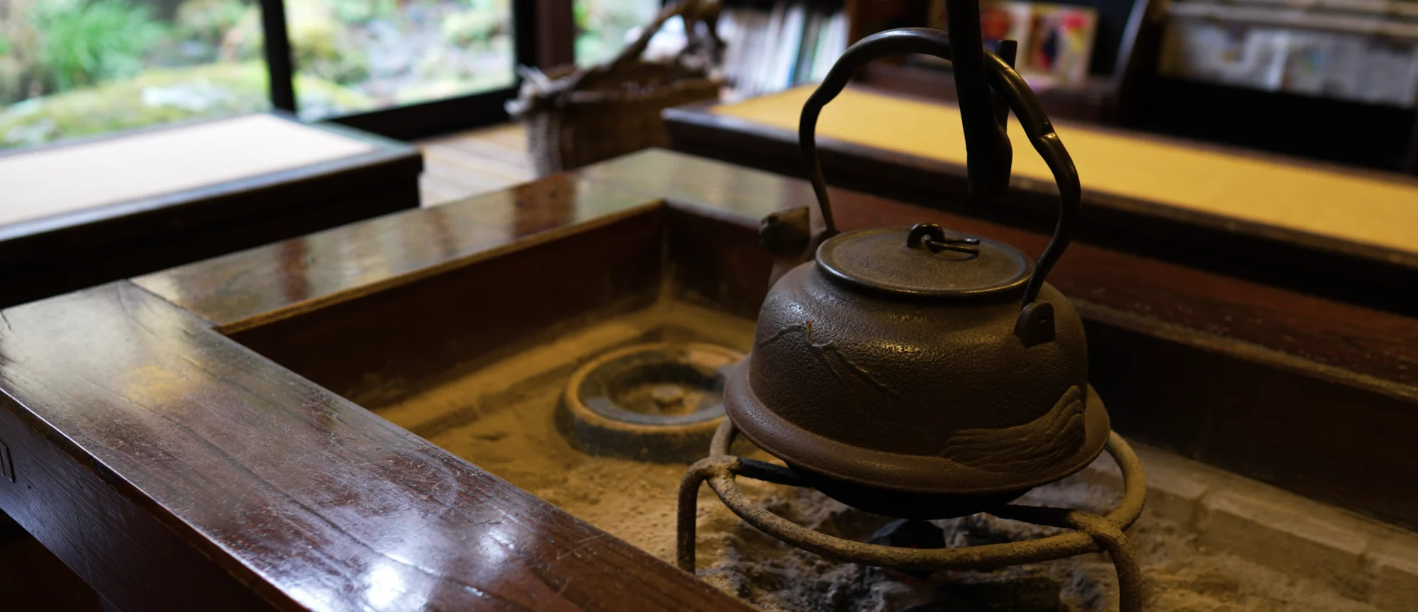 A cast-iron kettle hanging above a sunken irori hearth in a polished timber floor