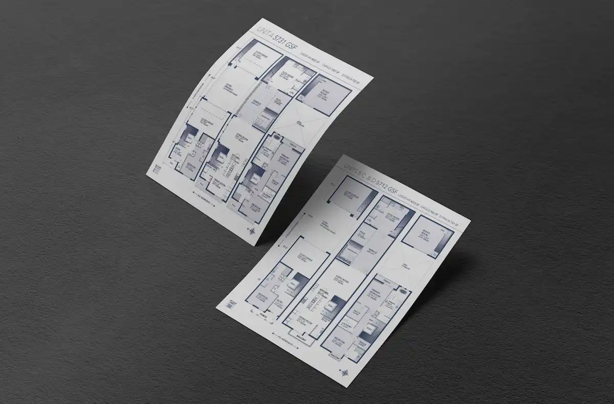 Two architectural floor plans displayed on angled sheets of paper against a dark textured background. The blueprints showcase layouts for luxury residential units, detailing room dimensions, garage spaces, and living areas with a clean, professional design aesthetic.