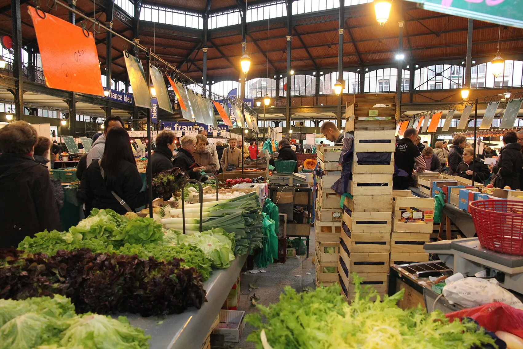 Marché couvert animé avec étals de légumes frais et clients. Ambiance de marché traditionnel. Vente de produits frais.