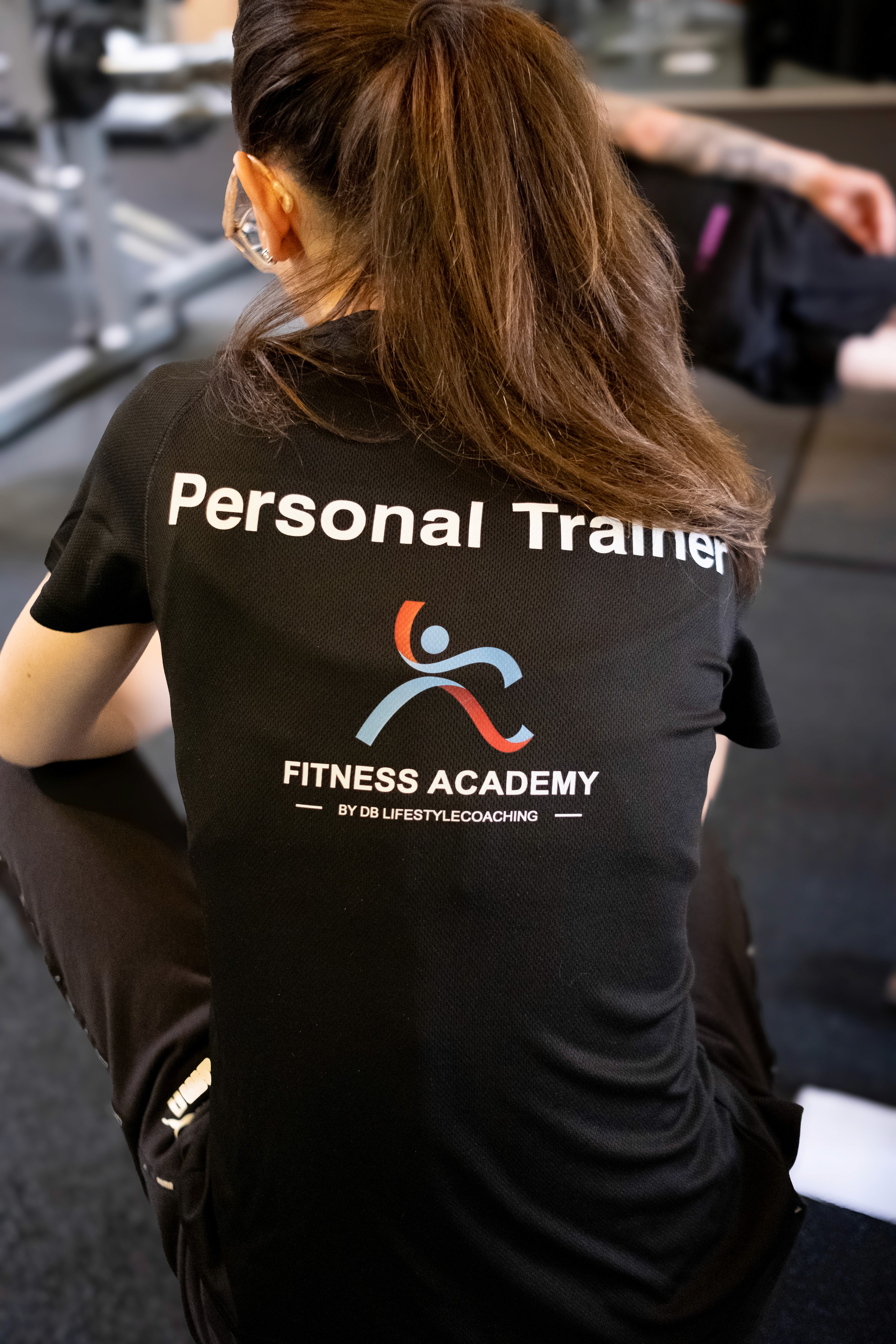 Personal trainer in a Fitness Academy shirt coaching a client in a gym