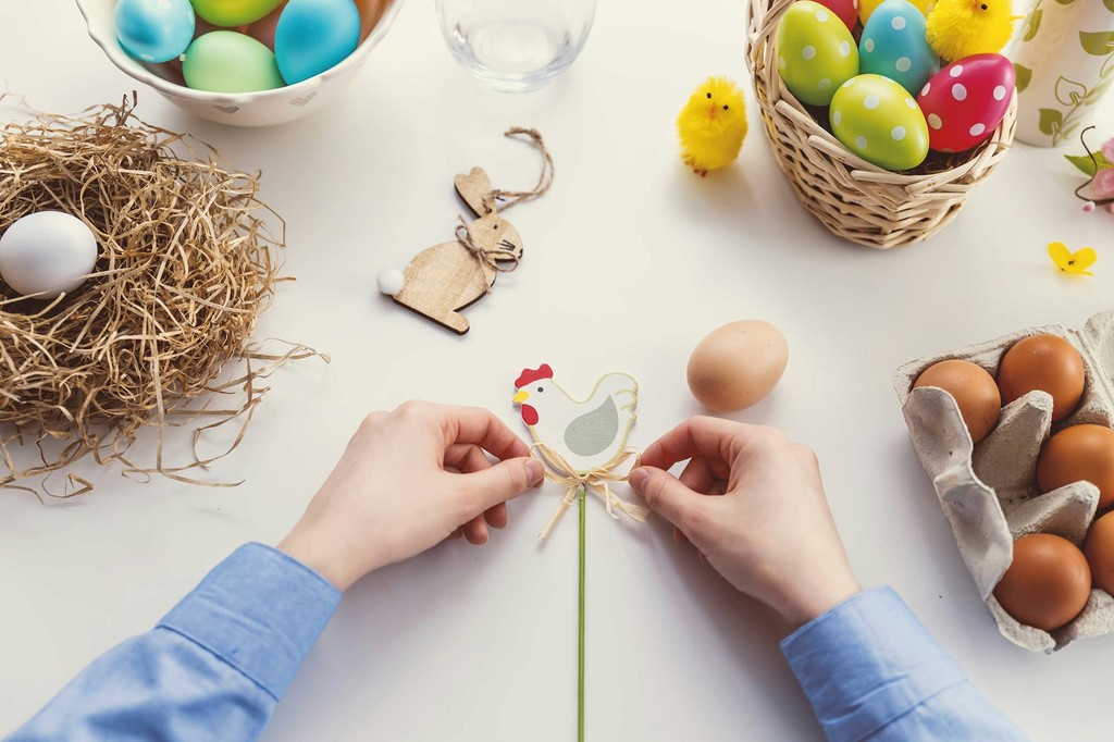 Hands arrange a decorative chicken stick amidst various egg products, including brown eggs in a carton and colorful.