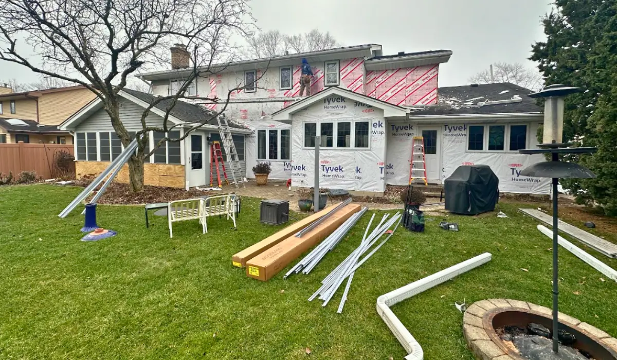 Contractor working on siding repairs vs. full replacement with Tyvek wrap covering residential home exterior walls.