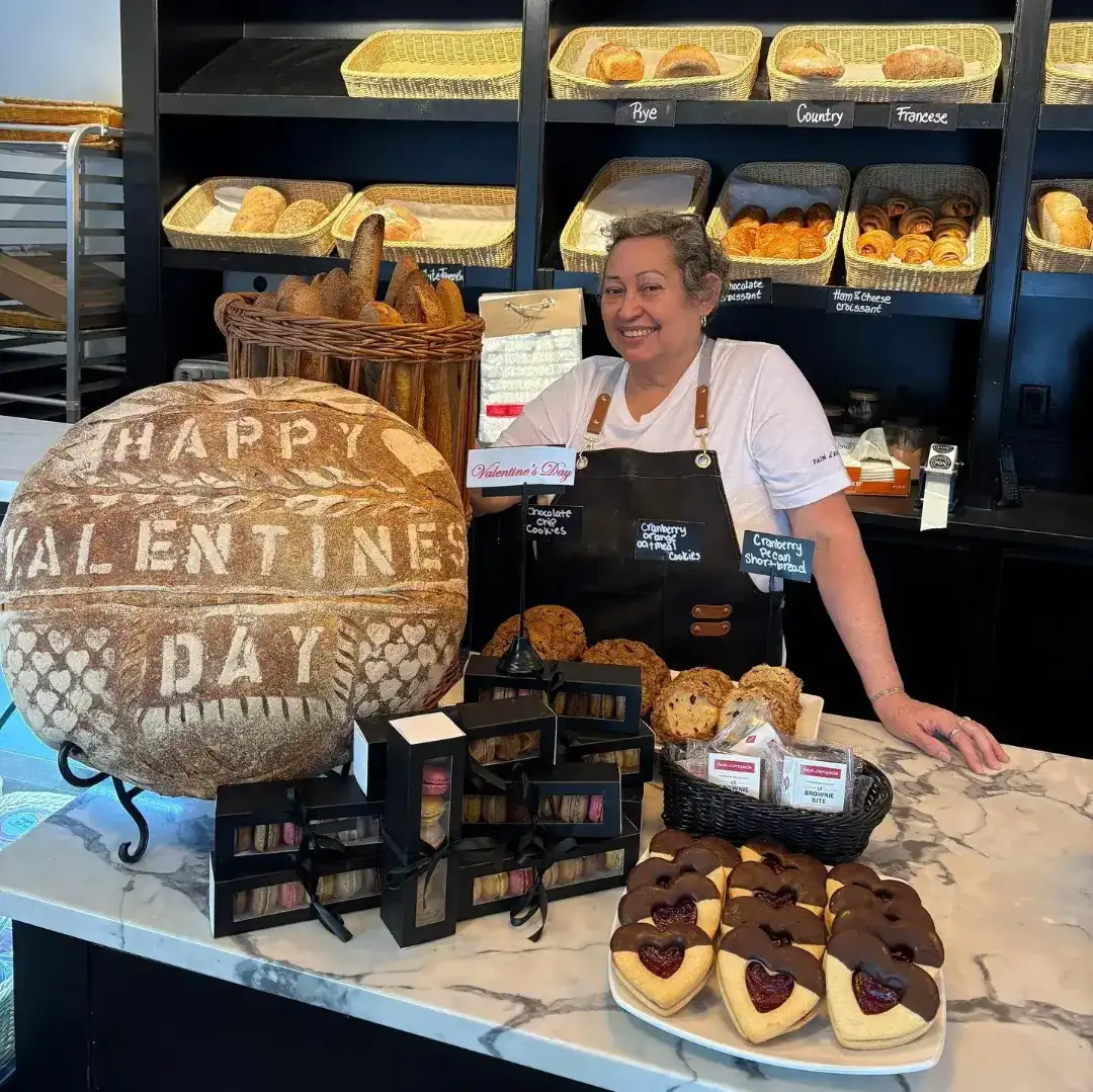 Pain D’Avignon bakery display featuring fresh pastries for Valentine's Day and smiling staff member.