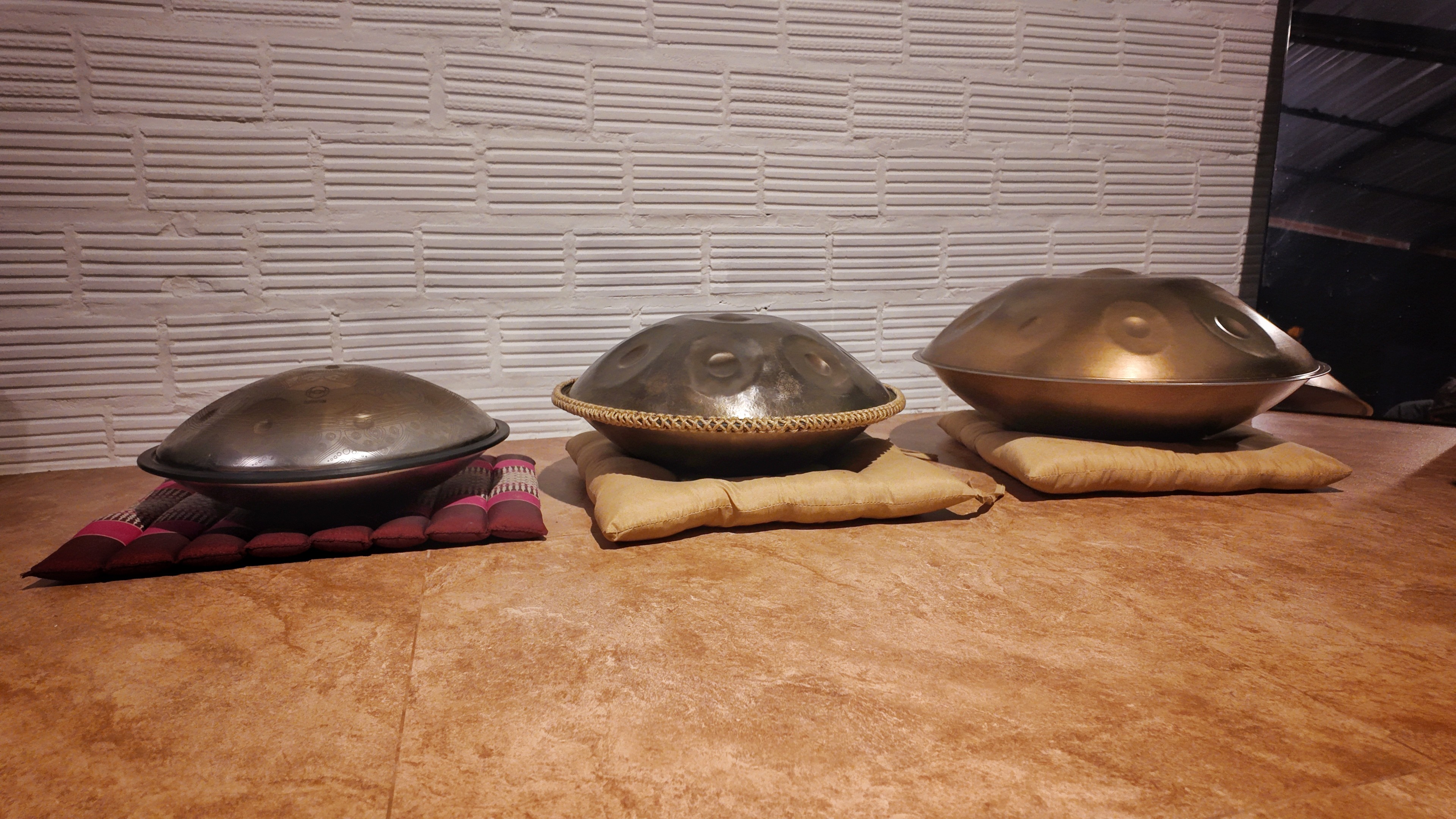 Three handpans of different sizes lie side by side on a mat on the floor.