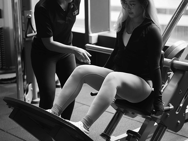 Man Woman Using A Leg Press Machine With A Female Personal Training Coach