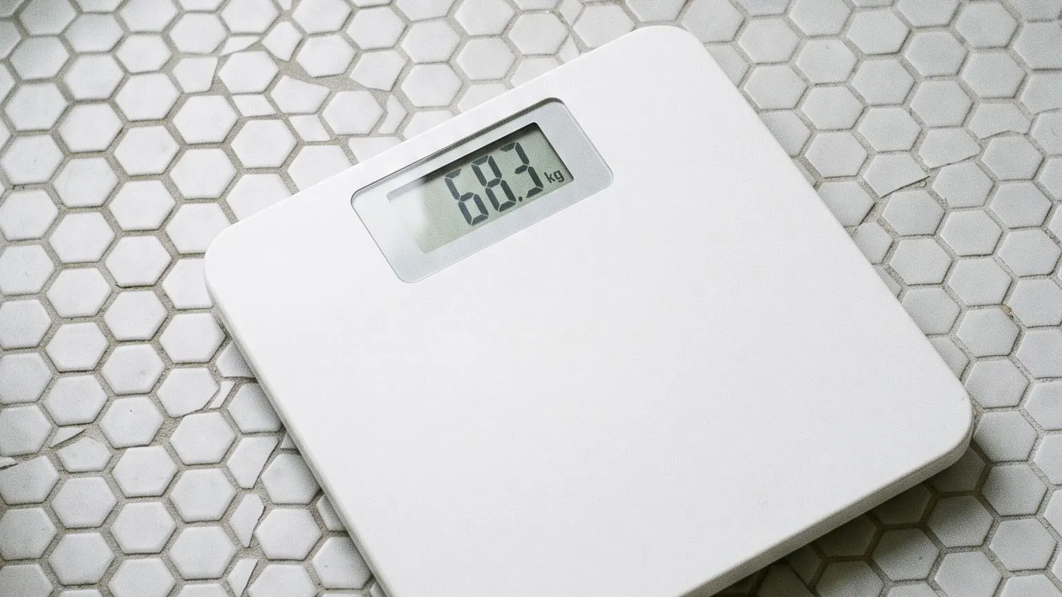 Seen from above, a bathroom scale on hexagonal tiles with its display showing a weight