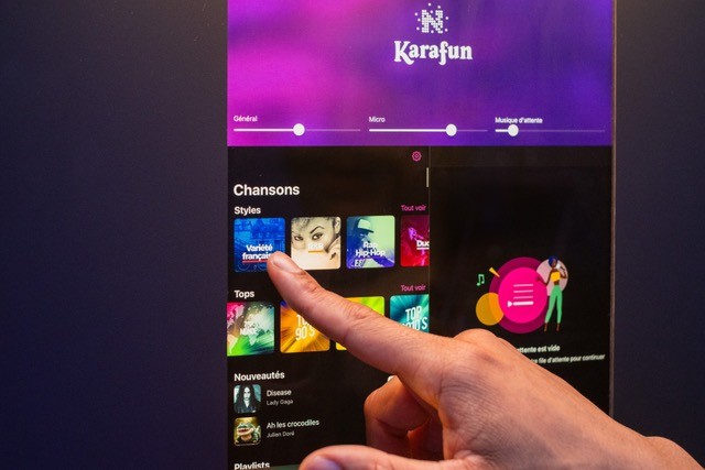 A young person with curly hair smiles at the camera while sitting in front of a laptop against a dark background.