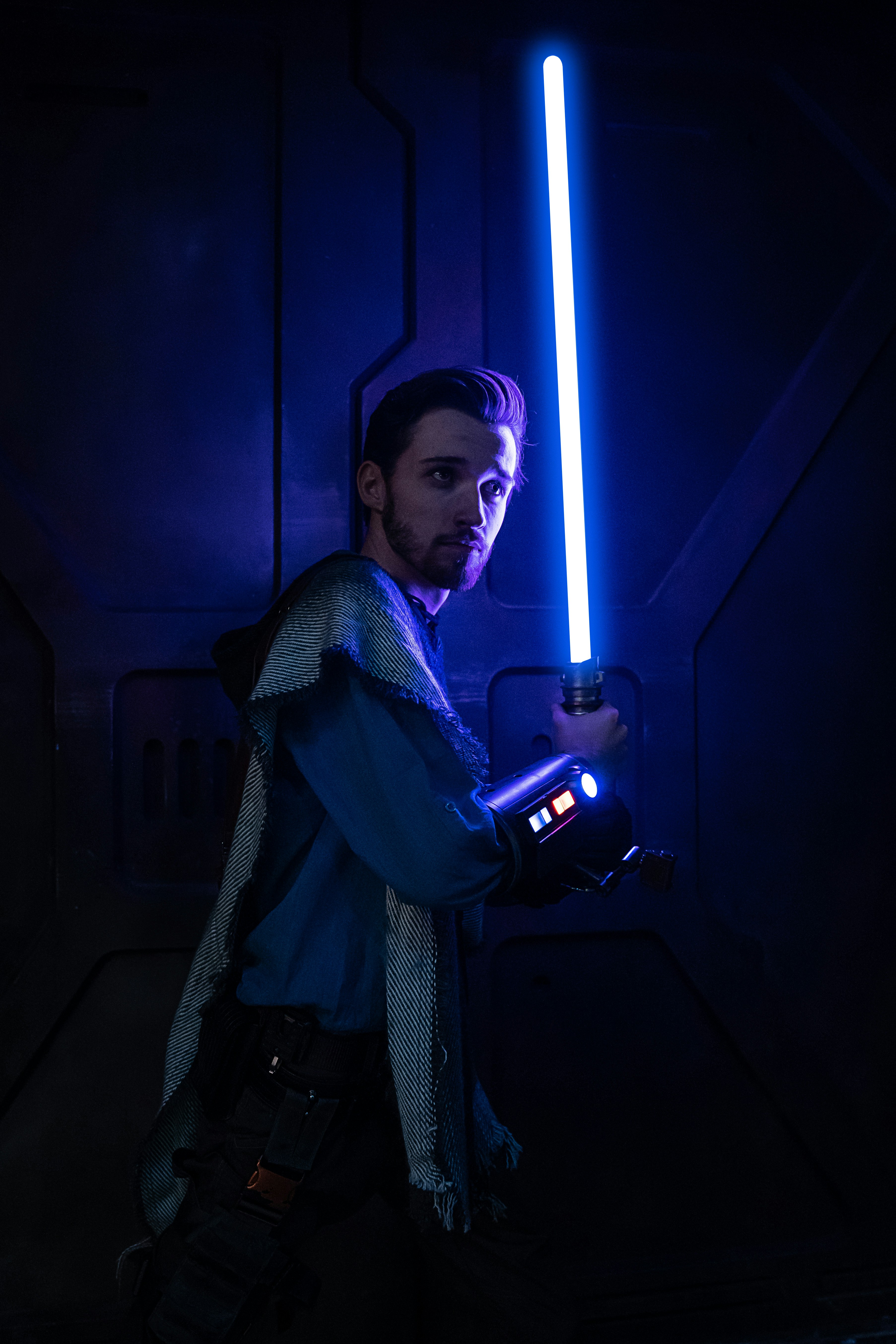 A man in cosplay as a Jedi Knight carrying a blue lightsabre