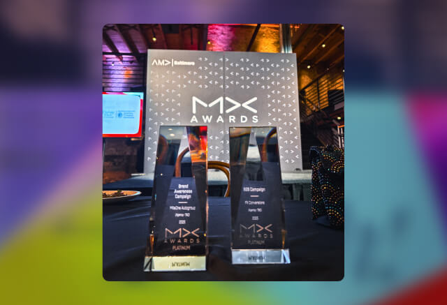 Two clear MX Awards trophies displayed on a table, with an MX Awards sign and digital screens visible in the background.