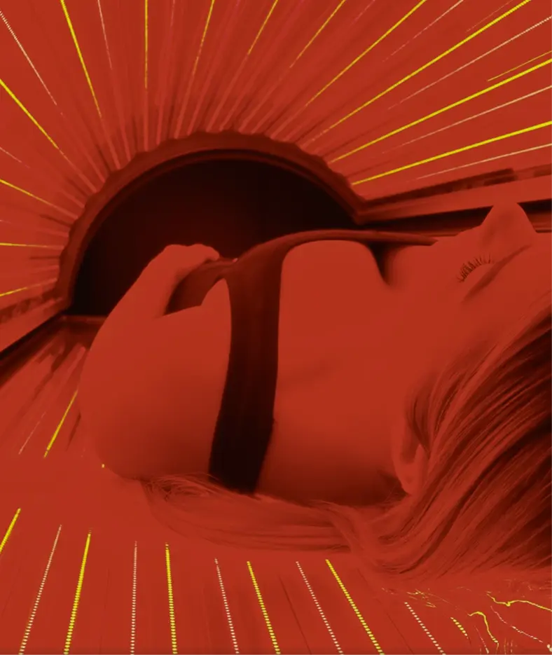 A person lying in a high-tech tanning bed with glowing orange and yellow lights, creating a warm and luxurious atmosphere, ideal for a premium fitness and wellness spa experience.