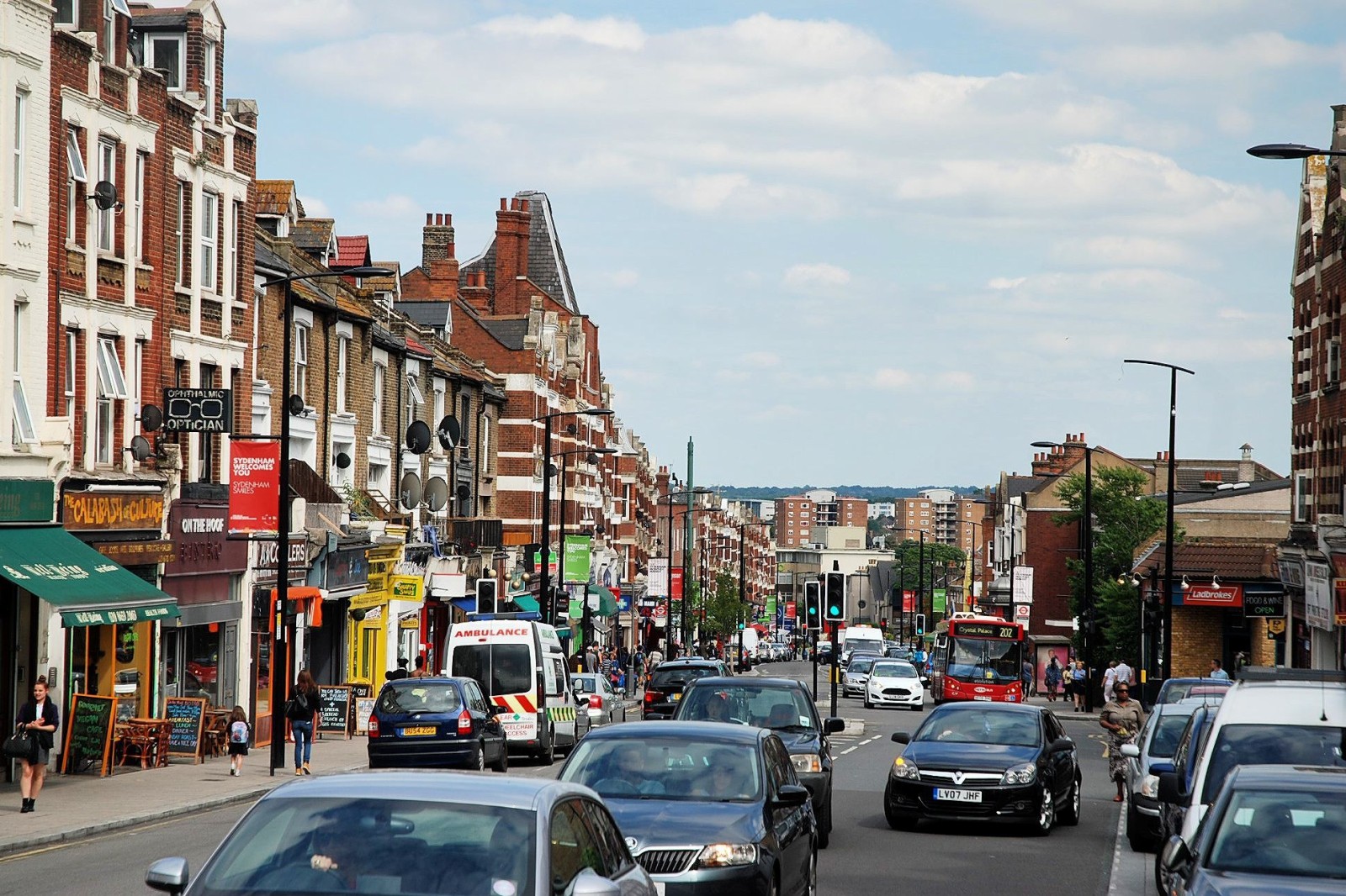 A smiling man with curly hair is sitting at a desk, looking at the camera, with a laptop and a lamp in the background.