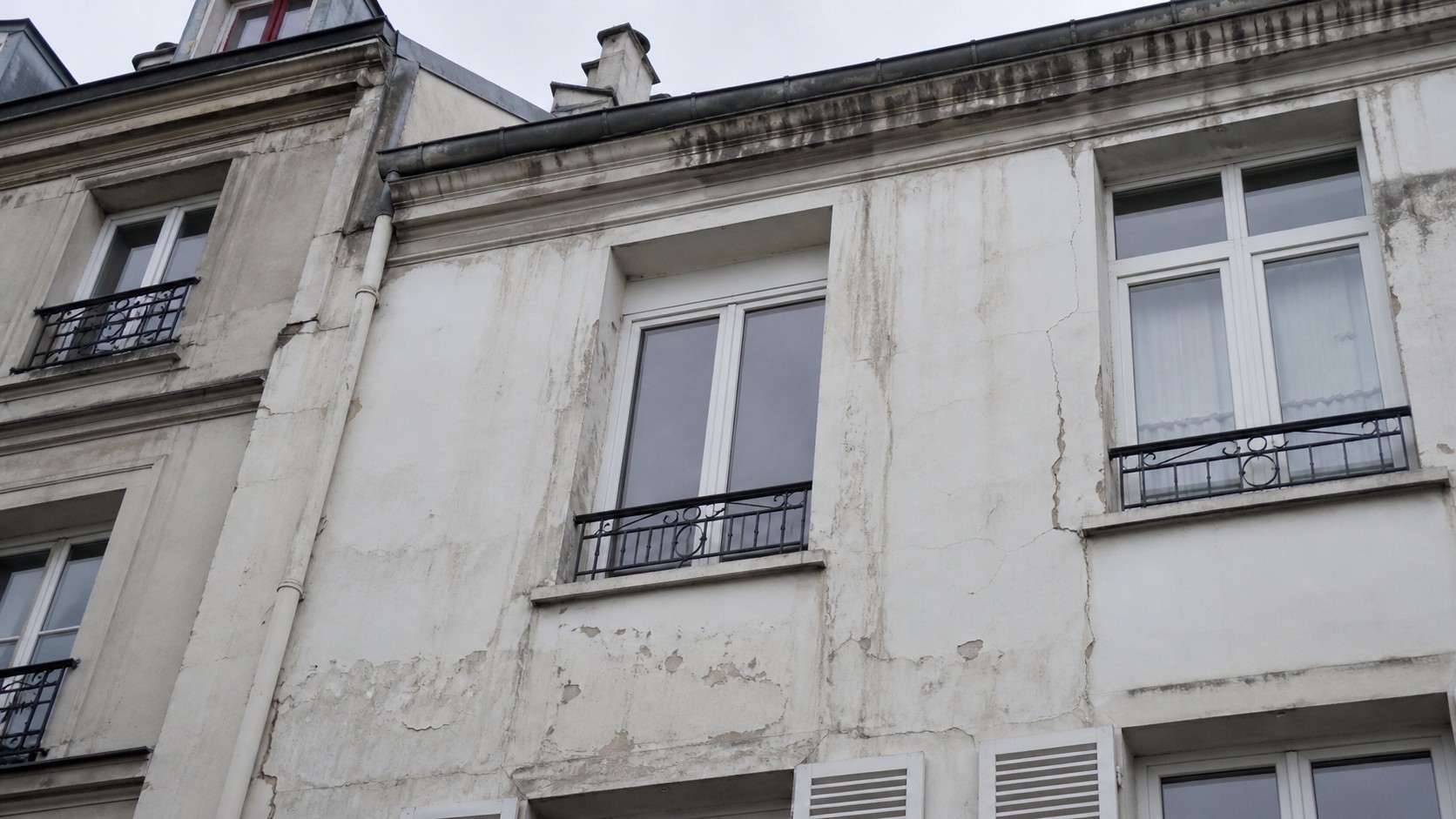 Photo réaliste d’une façade d’immeuble parisien avec traces d’infiltration, fissures, peinture écaillée et humidité autour des fenêtres pour diagnostic bâtiment.