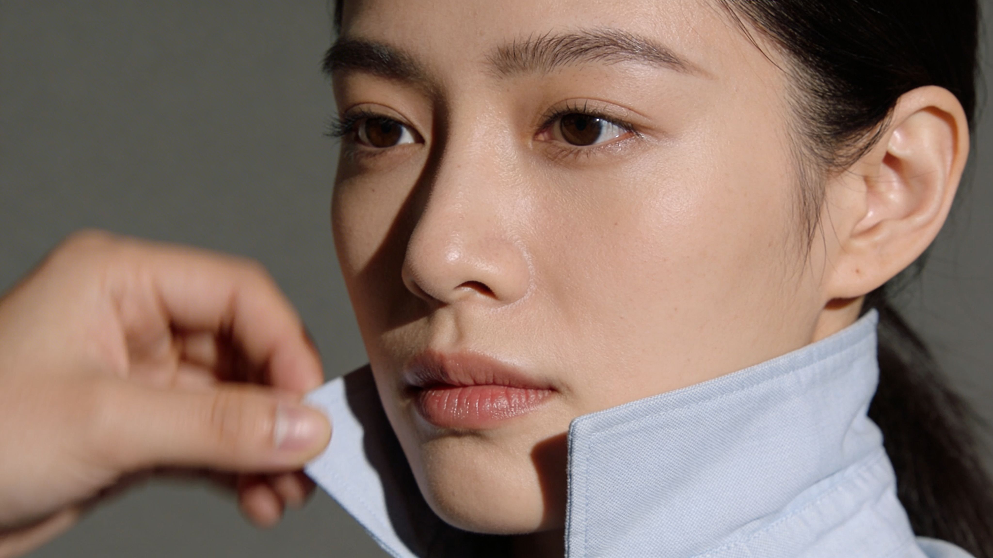 Eine Person richtet den Kragen einer hellblauen Bluse am Hals einer jungen asiatischen Frau im Profil.