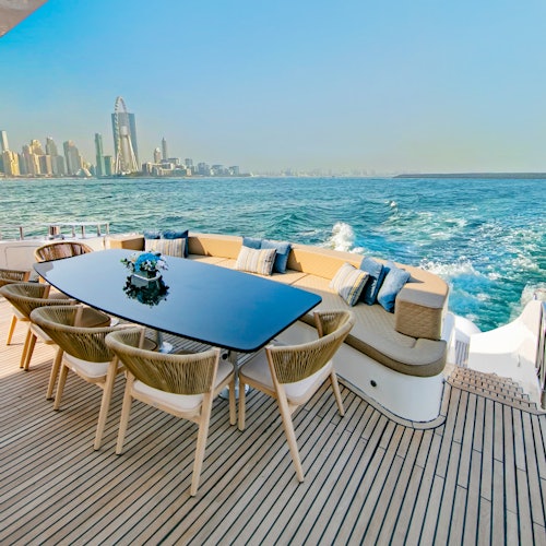 豪華遊艇的甲板上有一張桌子，周圍擺放著椅子，還有內置座椅，背景是城市天際線和海浪。