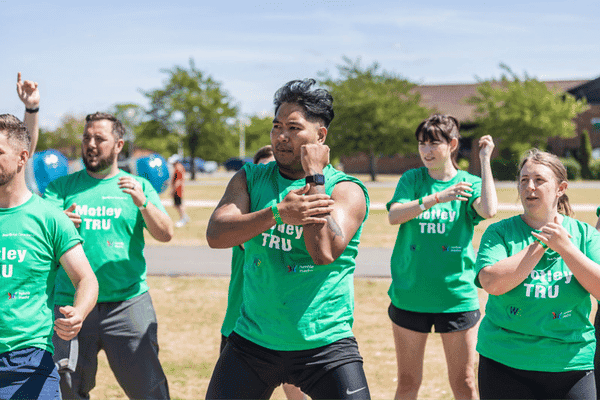 Outdoor team-building event with participants wearing matching blue shirts, taking part in inflatable obstacle courses and games, smiling and cheering, with the words 'ENTER A TEAM' in large bold white and green text across the image.