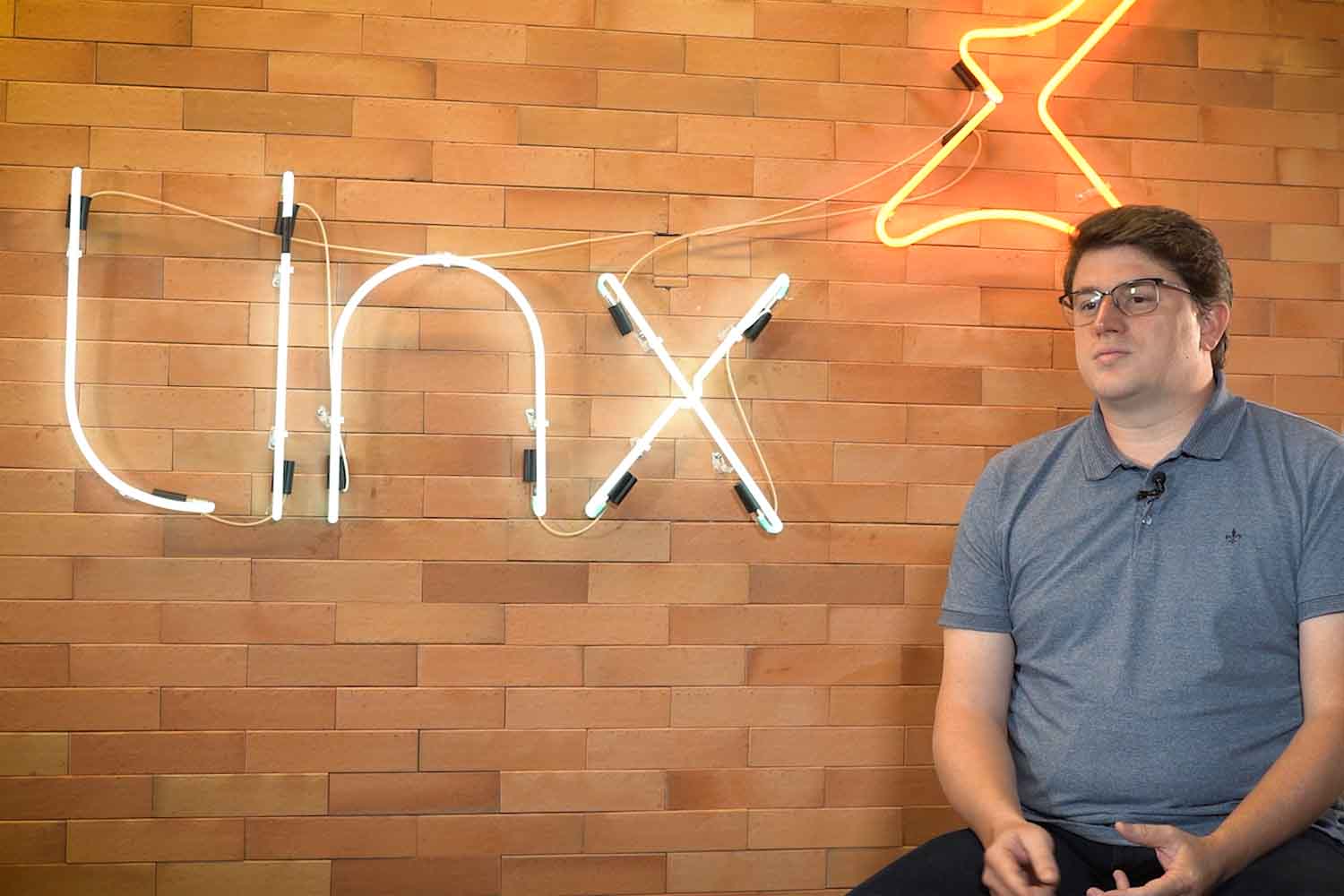 Profissional de TI concedendo entrevista em frente à logomarca em neon da Linx, empresa de tecnologia para o varejo